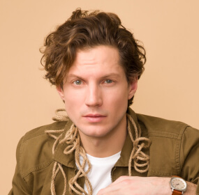 Hombre de cabello rizado con cuerdas alrededor del cuello, fondo beige.