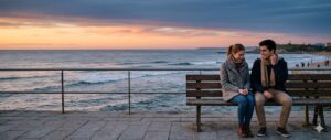 Pareja conversando en un banco frente al mar durante el atardecer.